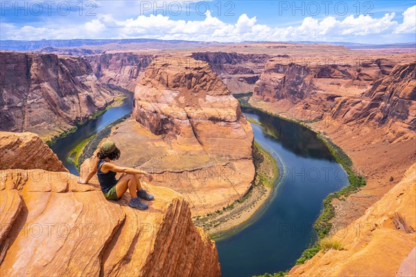 A tourist sitting on Horseshoe Bend and the Colorado River in the background