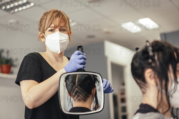 Hairdresser with a mask showing the client the haircut in a mirror. Reopening with security measures of Hairdressers in the Covid-19 pandemic