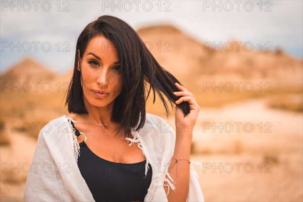 Sensual look of a young brunette Caucasian girl in a white dress sitting in a beautiful desert