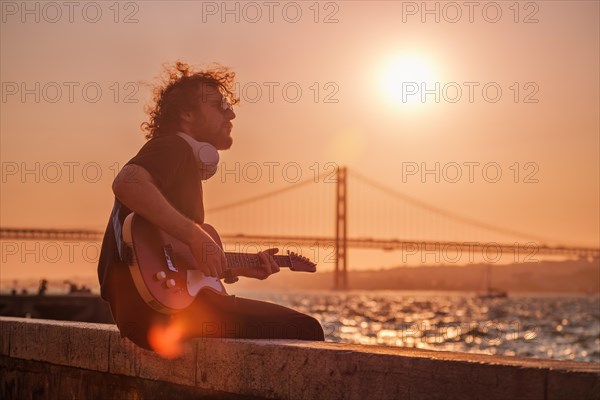 Hipster street musician in black playing electric guitar in the street on sunset