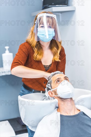 Hairdressers after the Coronavirus pandemic. Caucasian hairdresser with face mask and protective screen