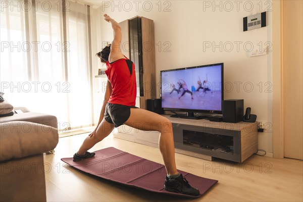 A young woman doing stretching in the room following the instructions of the online teacher. Sport in the covid19 quarantine at home