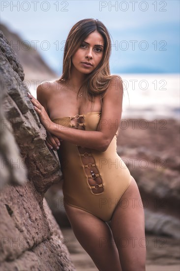 Portrait of a brunette woman with a swimsuit on the rocks of a beach in summer