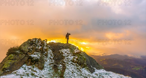 A young man on top of the mountain in the snowy winter orange sunset