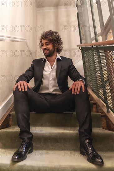Street style with a young dark-haired caucasian man in a black suit and a white shirt in a luxurious hotel