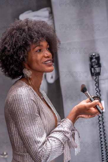 A young black girl with afro hair putting on makeup before the party with a smile. Exclusive party