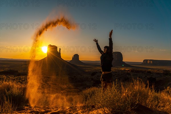 A brunette lifestyle girl at the dawn of Monument Valley playing with the red sand
