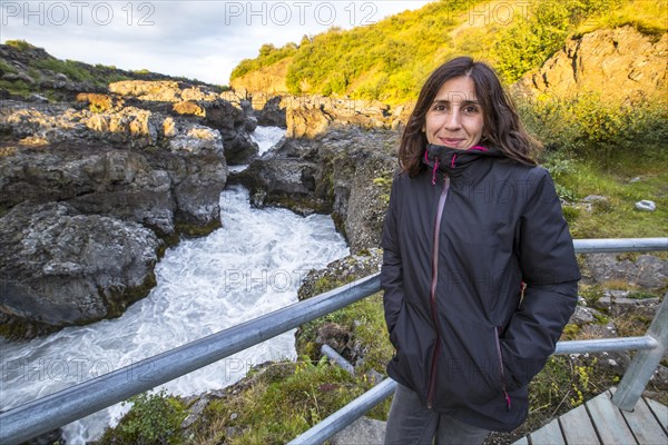 A woman in sunset seen from the wooden bridge of the Barnafoss river