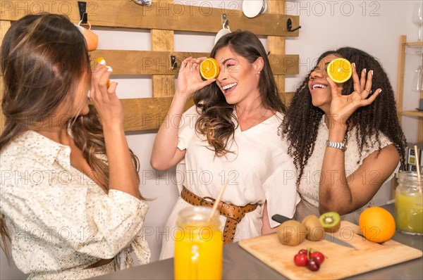 Beauty multi-ethnic friends having fun preparing healthy juice playing with fruits