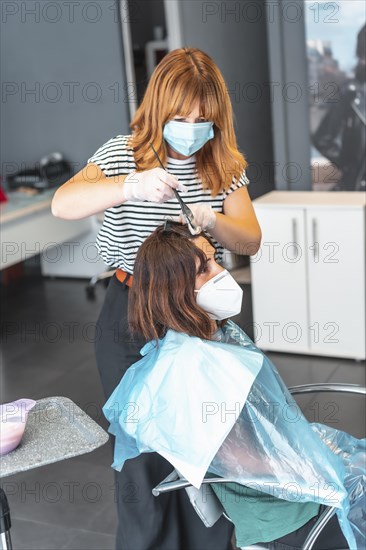 Hairdresser with mask dyeing gray hair to the client. Safety measures for hairdressers in the Covid-19 pandemic. New normal