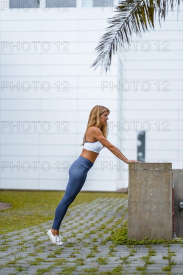 Fitness and yoga session with a young blonde Caucasian instructor dressed in a casual outfit with blue Maya and a white T-shirt. Performing stretches before starting the exercise