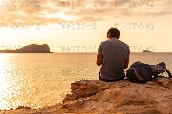 A tourist sitting watching the sunset at Cala Comte beach on the island of Ibiza. Balearic