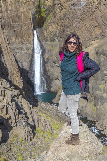 A young woman looking at the waterfall above Hengifoss from above. Iceland