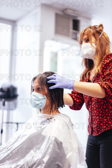 Hairdresser with mask and gloves showing the result to the client. Reopening with security measures for hairdressers in the Covid-19 pandemic