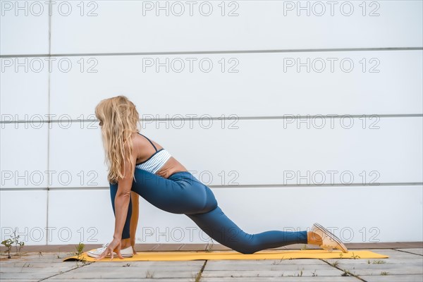 Yoga with blonde caucasian girl exercising on a yellow mat with a white wall in the background