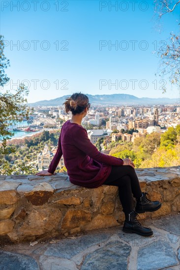 A young tourist sitting in spring looking at the views of the city and the Cathedral of the Incarnation of Malaga from the Castillo de Gibralfaro in the city of Malaga