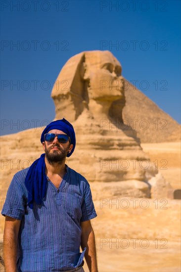 Portrait of a young tourist dressed in blue and a blue turban at the Great Sphinx of Giza. Cairo