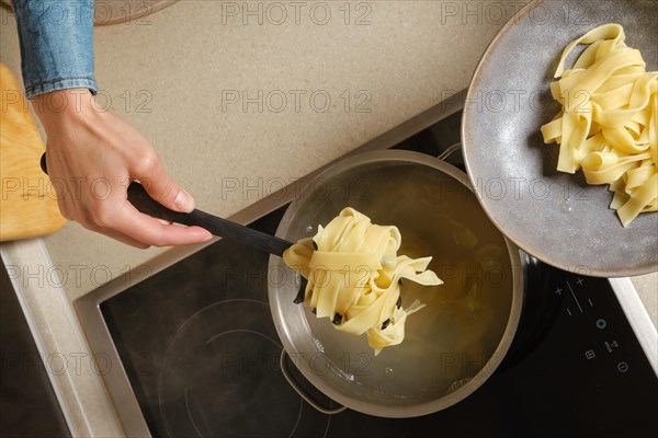 Top view of female hand taking cooked fettuccine pasta out of the saucepan