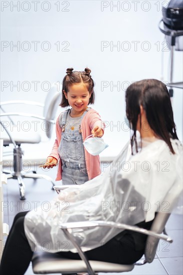 Client sitting waiting for the dye to dry and winged her daughter playing with the mask. Reopening with security measures for hairdressers in the Covid-19 pandemic