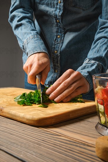 An unrecognizable woman cuts parsley into large pieces