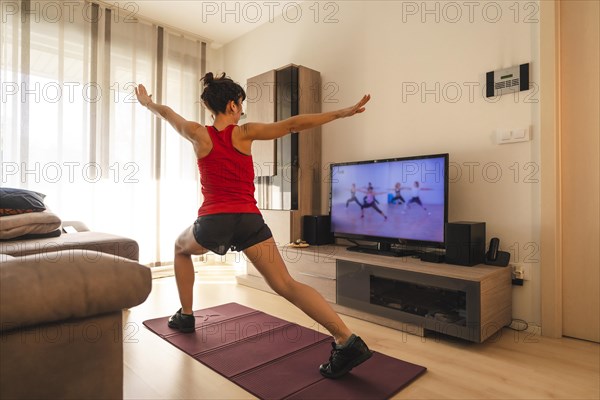 A young woman doing stretching in the room following the instructions of the online teacher. Sport in the covid19 quarantine at home