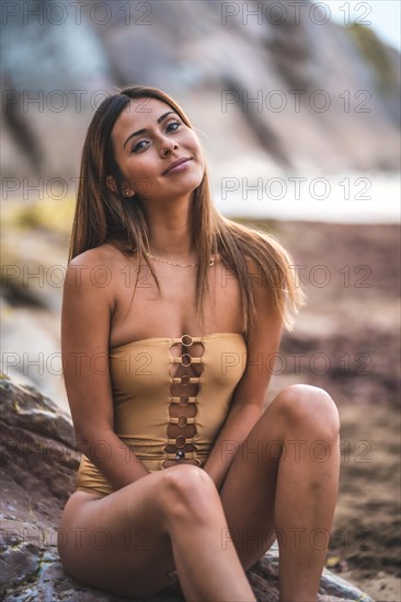 Portrait of a brunette woman smiling with a swimsuit on the rocks of the beach in summer