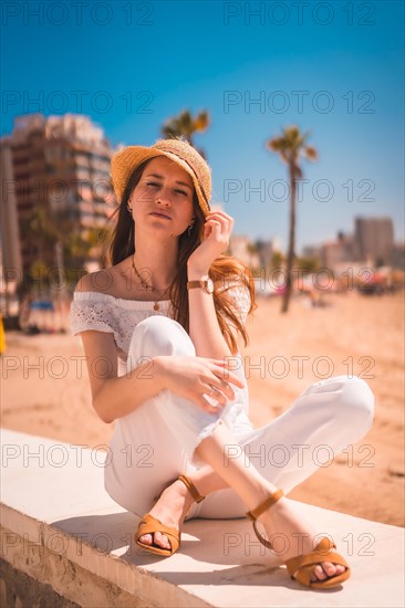 A young red-haired Caucasian girl dressed in white and with a straw hat on the beaches of Calpe