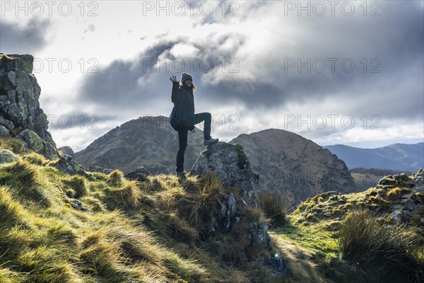 A young woman with a winter hat waving at the top on Mount Aiako Harria stacked on a stone