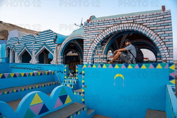 A young tourist sitting on a beautiful terrace of a traditional blue house in a Nubian village along the Nile river and near the city of Aswan. Egypt