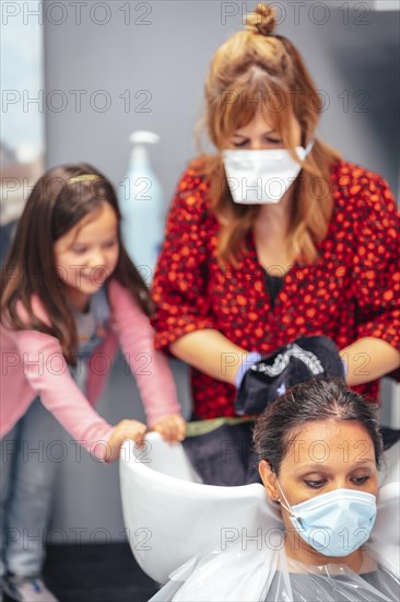 Hairdresser with mask and gloves washing the hair of the client and her daughter playing winged. Reopening with security measures for hairdressers in the Covid-19 pandemic