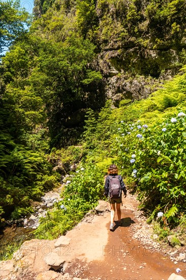 A young woman on the trail next to the waterfall at Levada do Caldeirao Verde