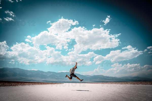 A young man jumping with a blue shirt on the white salt of Badwater Basin