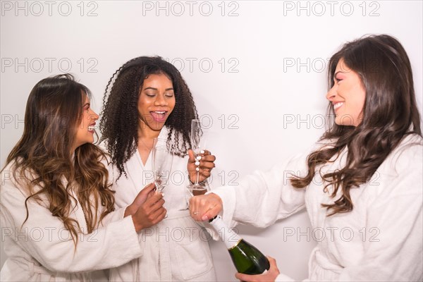 Studio photo with white background of three woman opening a bottle of champagne