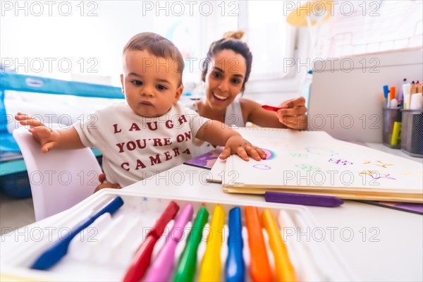 Young Caucasian mother playing with her in the room with toys. Baby less than a year learning the first lessons of her mother. Painting with color paints