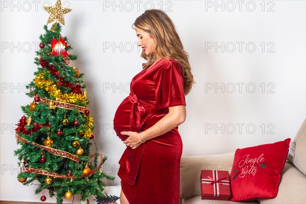Beautiful pregnant blonde Caucasian woman in a decorating with Christmas tree