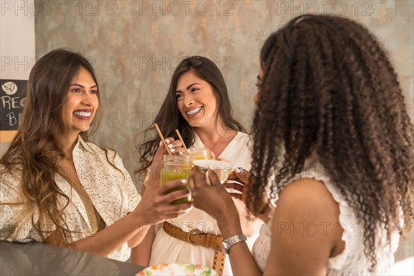 Three latin happy women toasting with juices in a cafeteria