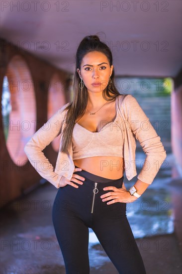 Young caucasian brunette in the city with a beautiful ponytail and a short pink sweater. Street style fashion