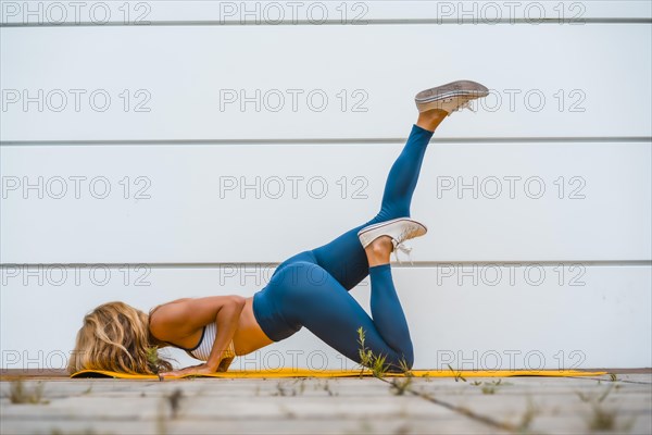 Fitness with blonde caucasian girl exercising on a yellow mat with white wall in the background