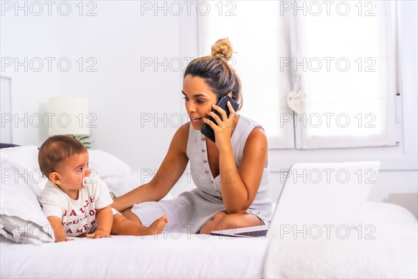 Young Caucasian mother with her son in the room on top of the bed. Mother teleworking and caring for her child