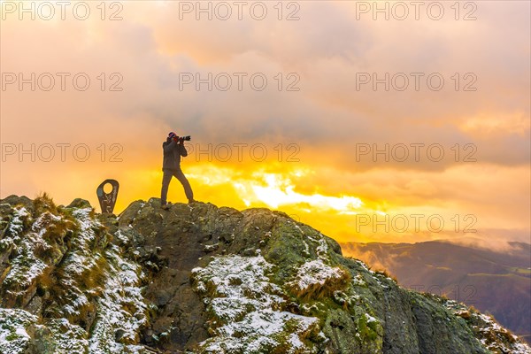 A photographer on top of the mountain in the snowy winter orange sunset