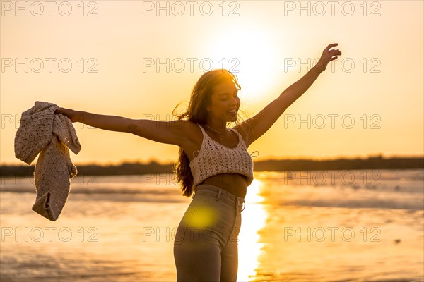 Summer lifestyle. A young blonde Caucasian woman in a white short wool sweater on a beach sunset. Enjoying the summer afternoon