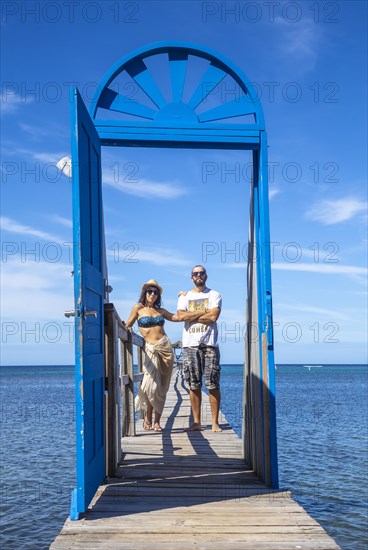 A couple at a blue door on the beach of Sandy Bay on Roatan Island. Honduras