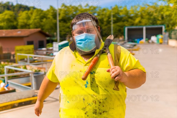 Worker in a recycling factory or clean point and garbage with a face mask and plastic protective screen