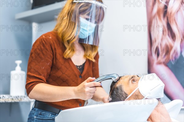 Reopening of hairdressing salons after the Coronavirus pandemic. Hairdresser with face mask and protective screen