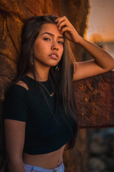 A young pretty brunette Latina with long straight hair in a short black T-shirt and pink pants. Portrait of the woman leaning on a sculpture with scab