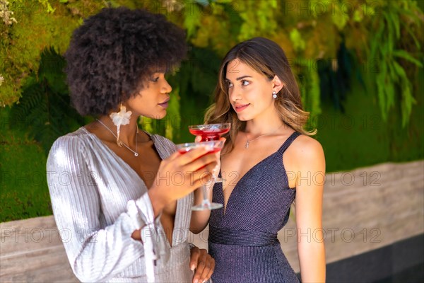 Two friends in gala dresses having a cocktail at a party in a hotel