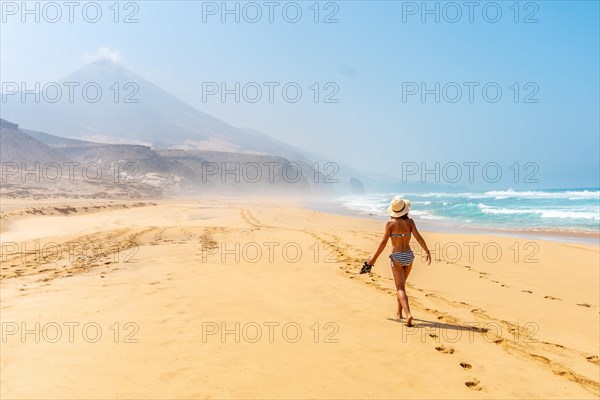 A young woman walking alone on the wild Cofete beach of the Jandia natural park