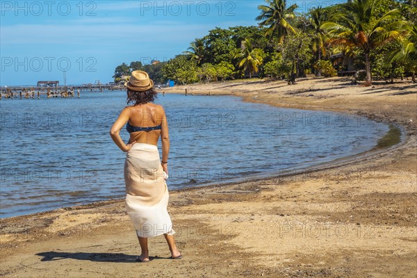 A young tourist in a bikini and skirt on the beach of Sandy Bay on Roatan Island looking at the Caribbean Sea. Honduras
