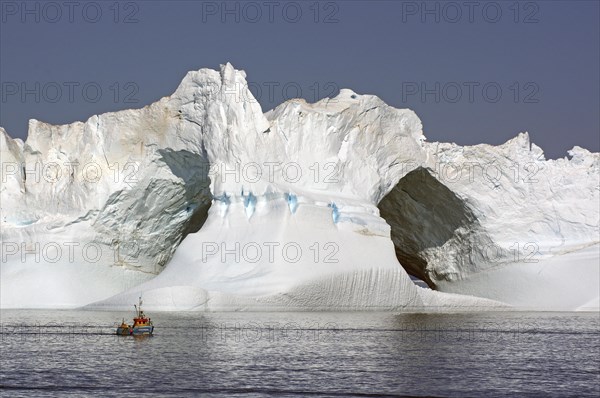 Small fishing boat in front of huge iceberg with large ice gates