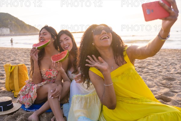 Friends waving while taking a selfie enjoying picnic on the beach during the sunset